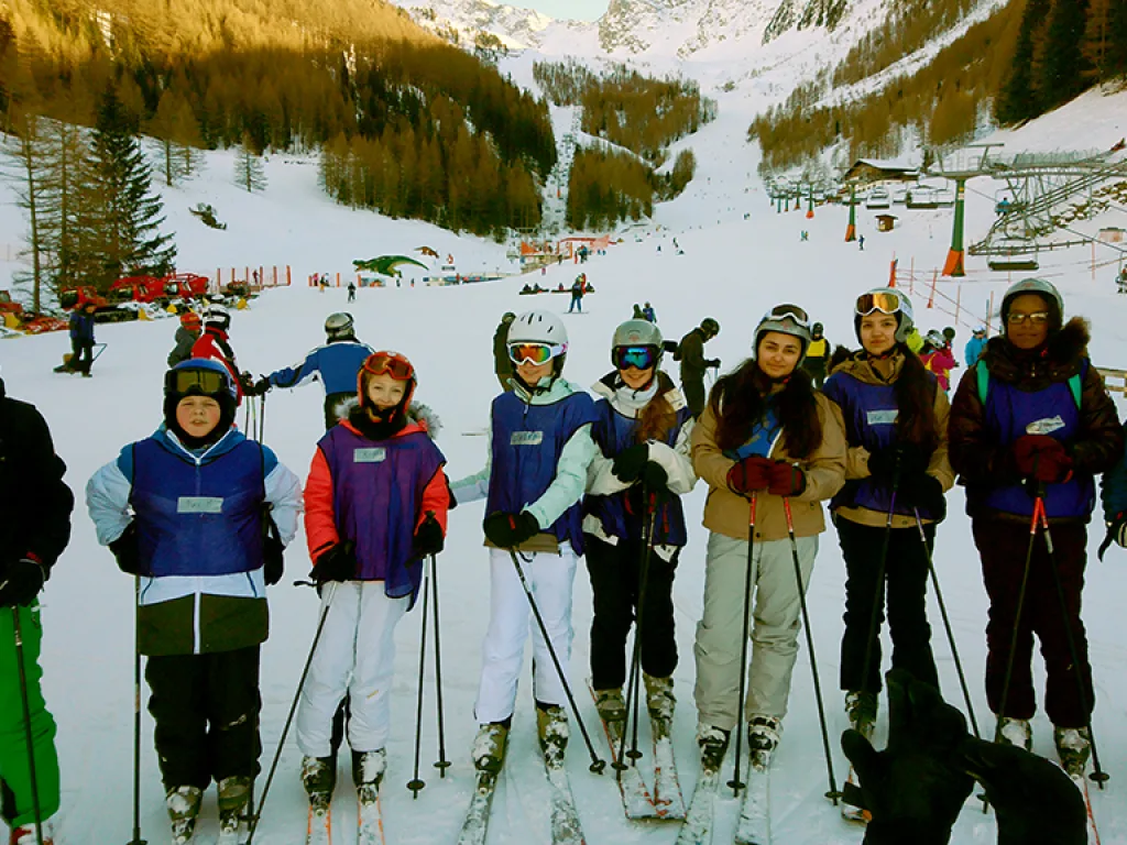 Skigruppe steht mit erhobenen Stöcken vor der Bergkulisse.